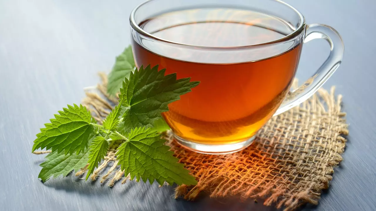 A cup of green tea with tea leaves beside it.